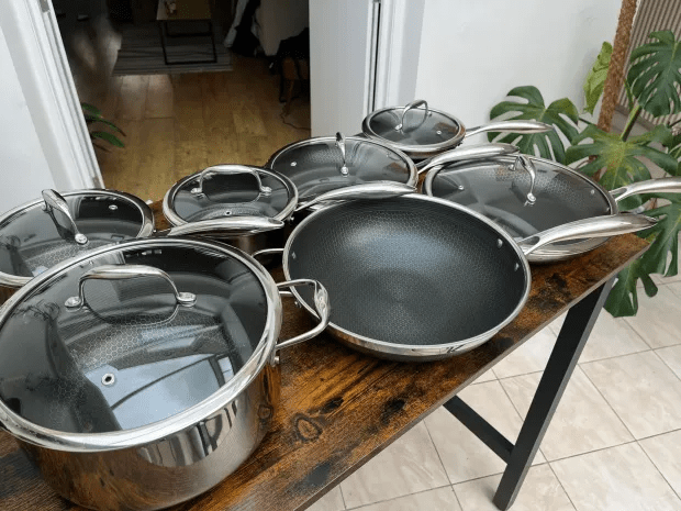 a row of pots and pans on a wooden table with a plant in the background