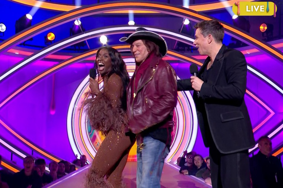 Mickey Rourke, AJ Odudu, and a host on a game show stage.