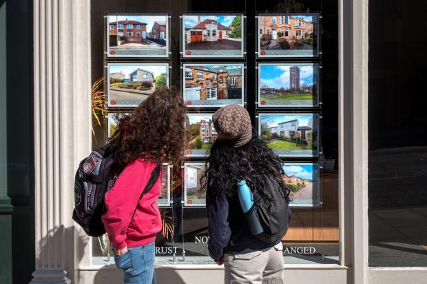 Two women looking at real estate listings in an estate agent's window.