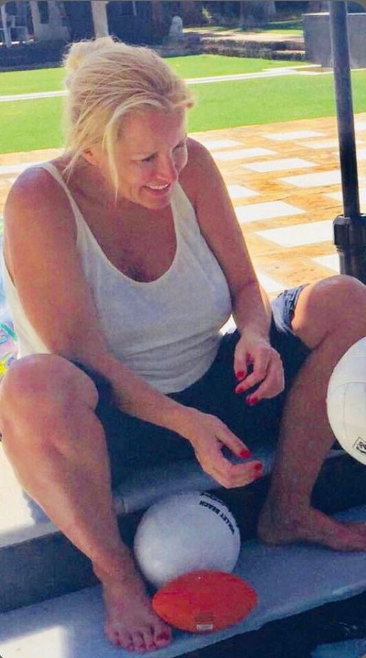 Woman sitting with volleyballs and a football.