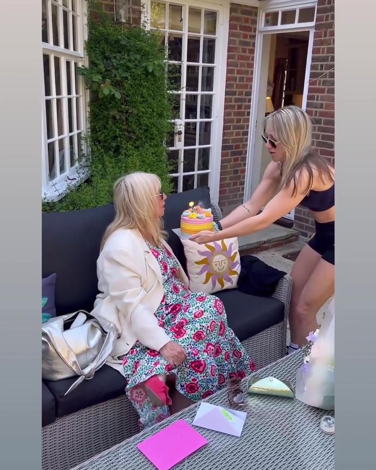 A daughter surprises her mother with a birthday cake outdoors.